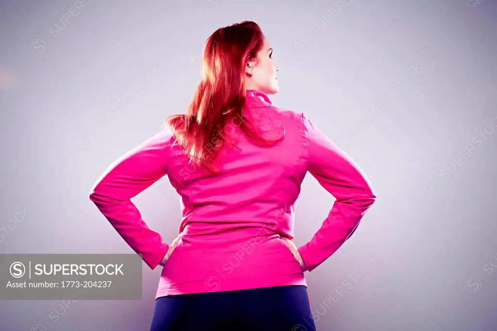 Young woman wearing pink top with hands on hips, rear view
