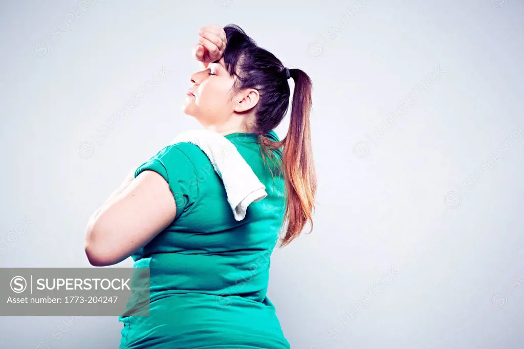 Mid adult woman wearing green t shirt, wiping brow