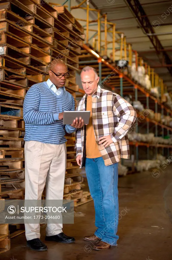 Male warehouse worker using digital tablet, pallets in background