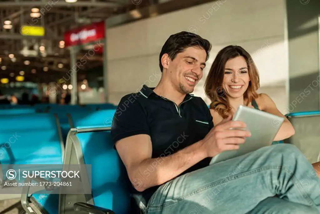 Young couple using digital tablet in airport departure lounge