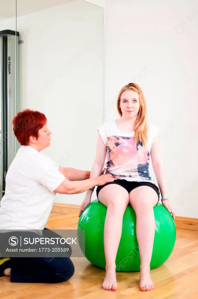 Young woman sitting on fitness ball, being guided by mature woman