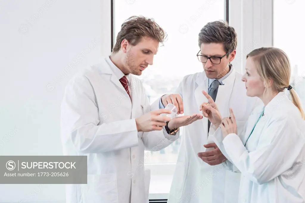 Three people wearing lab coats standing looking at contents of test tube