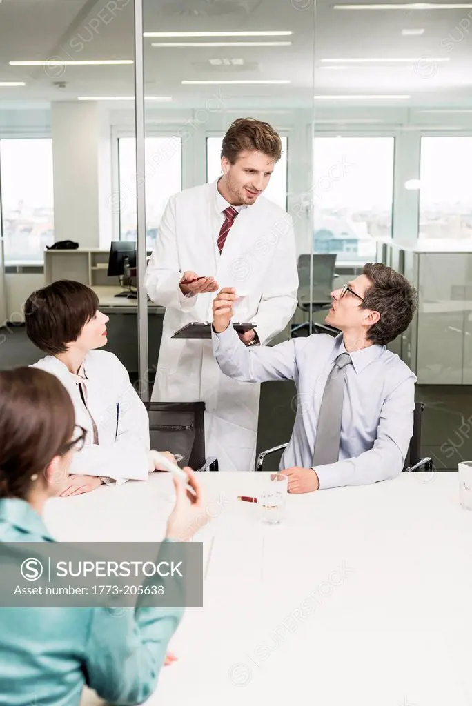 Man wearing lab coat standing behind colleagues sat at table