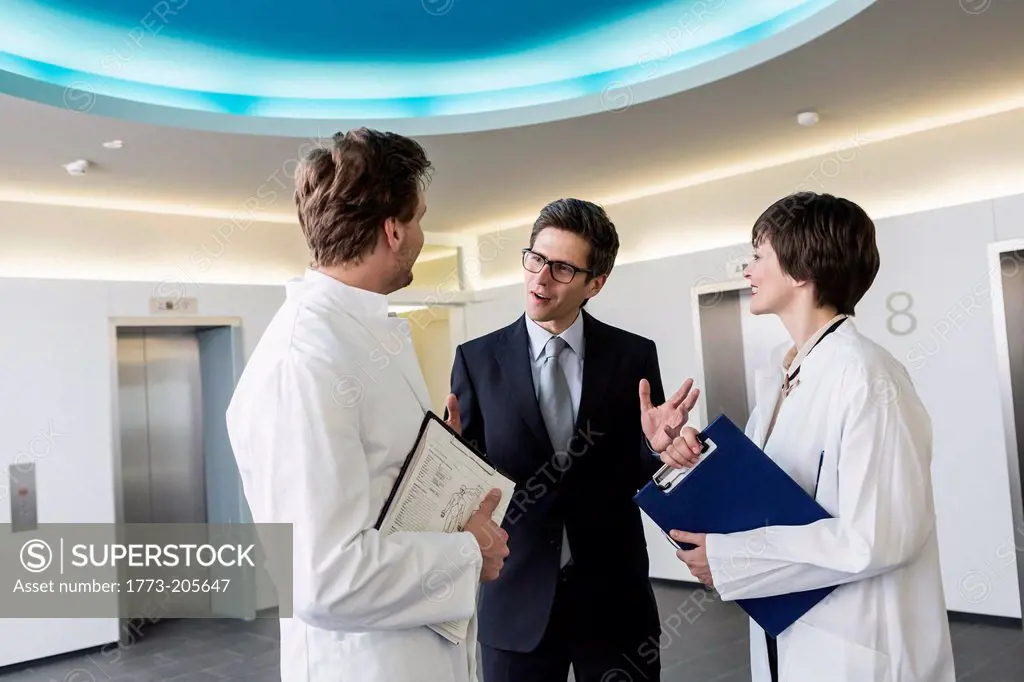 Man and woman wearing lab coats having conversation in lobby with man wearing business attire
