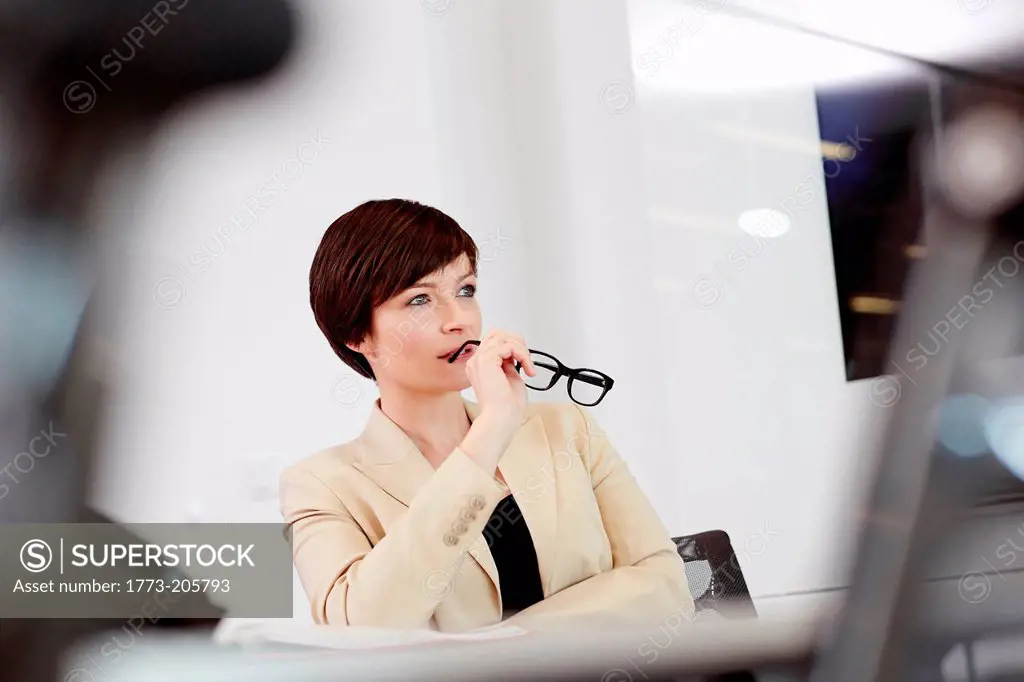 Businesswoman sitting in office chair holding eyeglasses to mouth