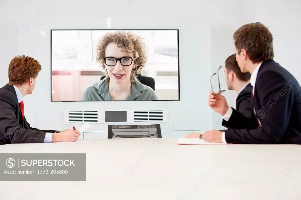 Businessmen sitting around conference table having video conference with woman