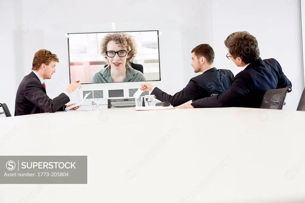 Businessmen sitting around conference table having video conference with woman