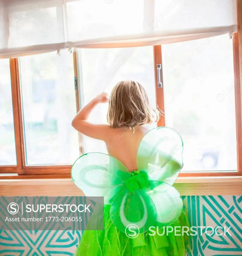 Back view of child in green fairy costume looking out window