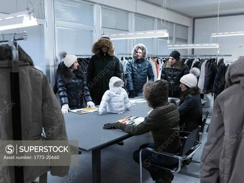 Cloned product developers inspecting toddler´s winter coat propped up on table in clothing manufacturer´s sample studio digital enhancement