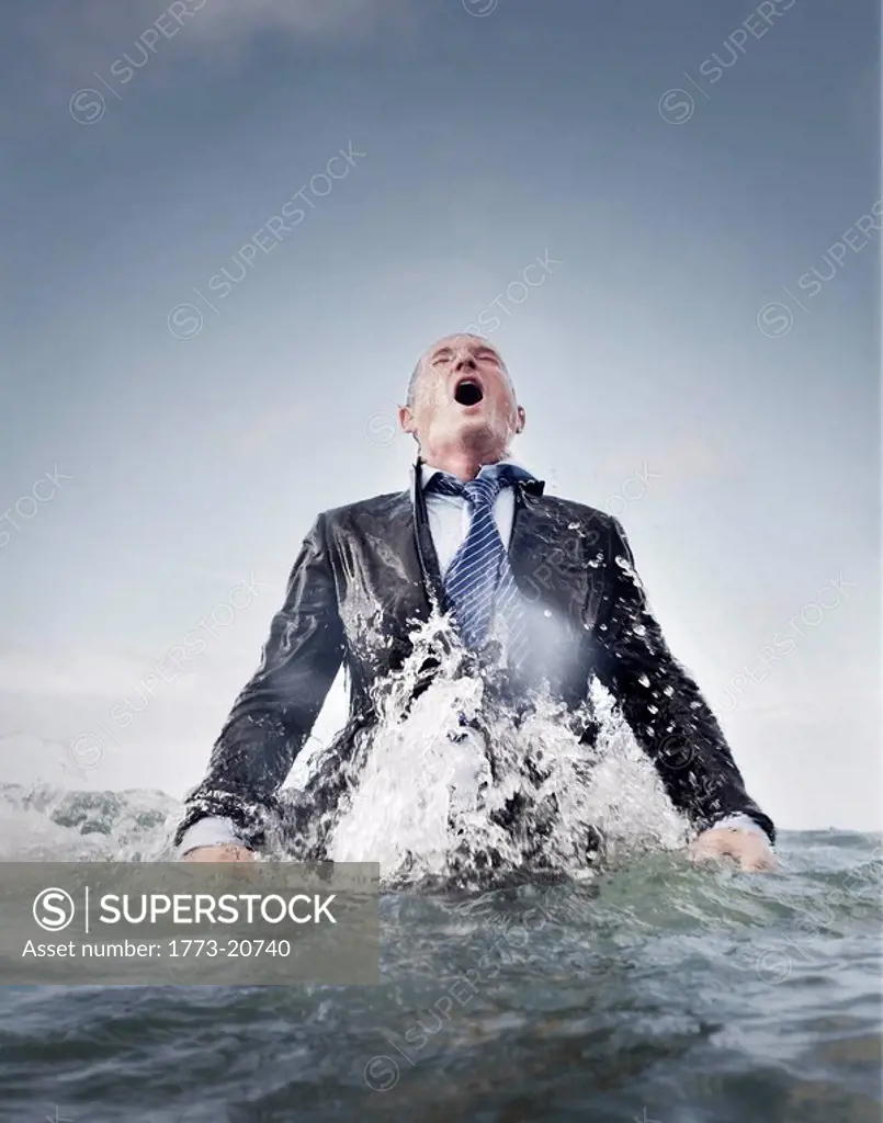 a businessman coming out of the sea for air, struggling.