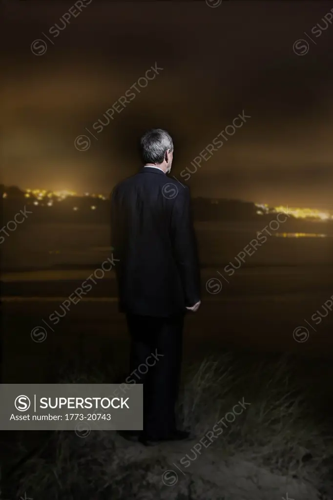 a businessman looking out in to the horizon, with the lights of a town in the background