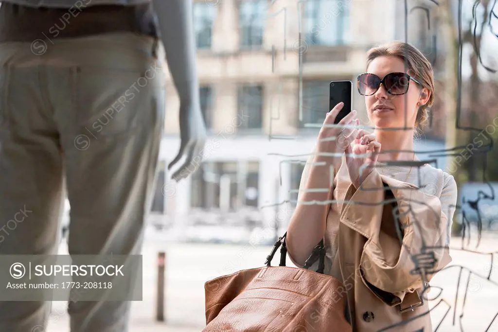 Young woman photographing fashion mannequin outside fashion shop