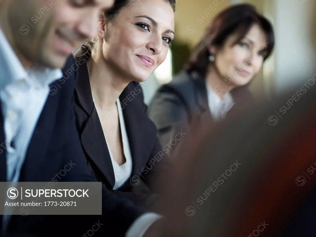 A portrait of a business woman engaging in a business meeting, people on in foreground and background.