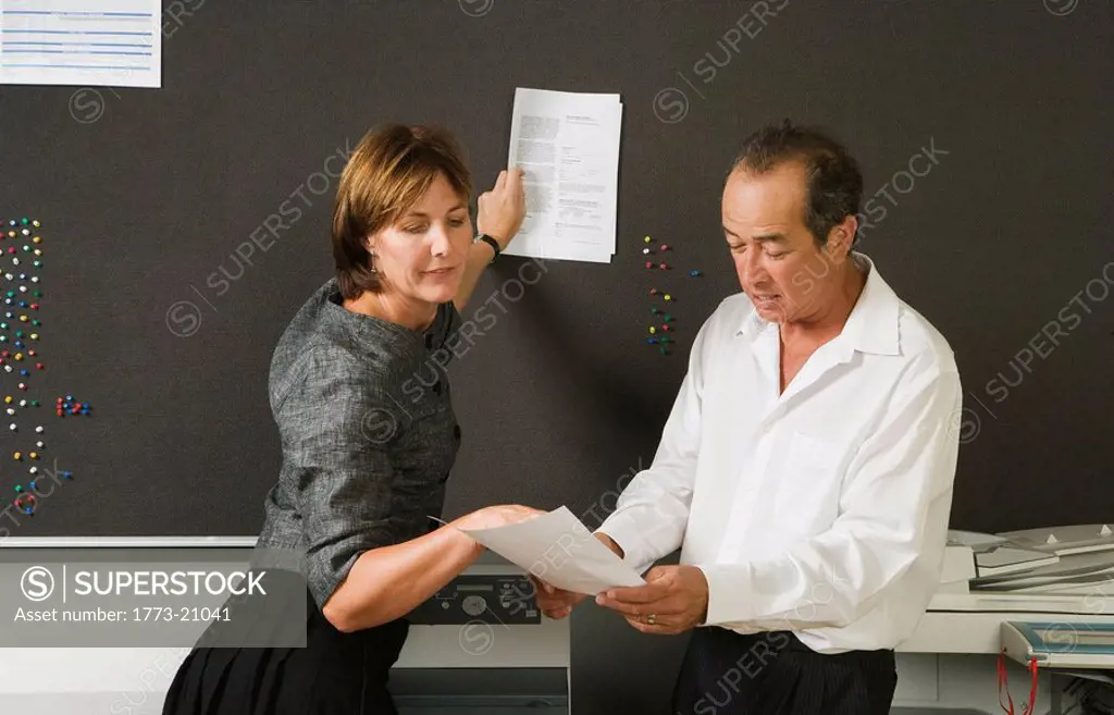 Work colleagues looking at notes and woman pinning paper to notice board