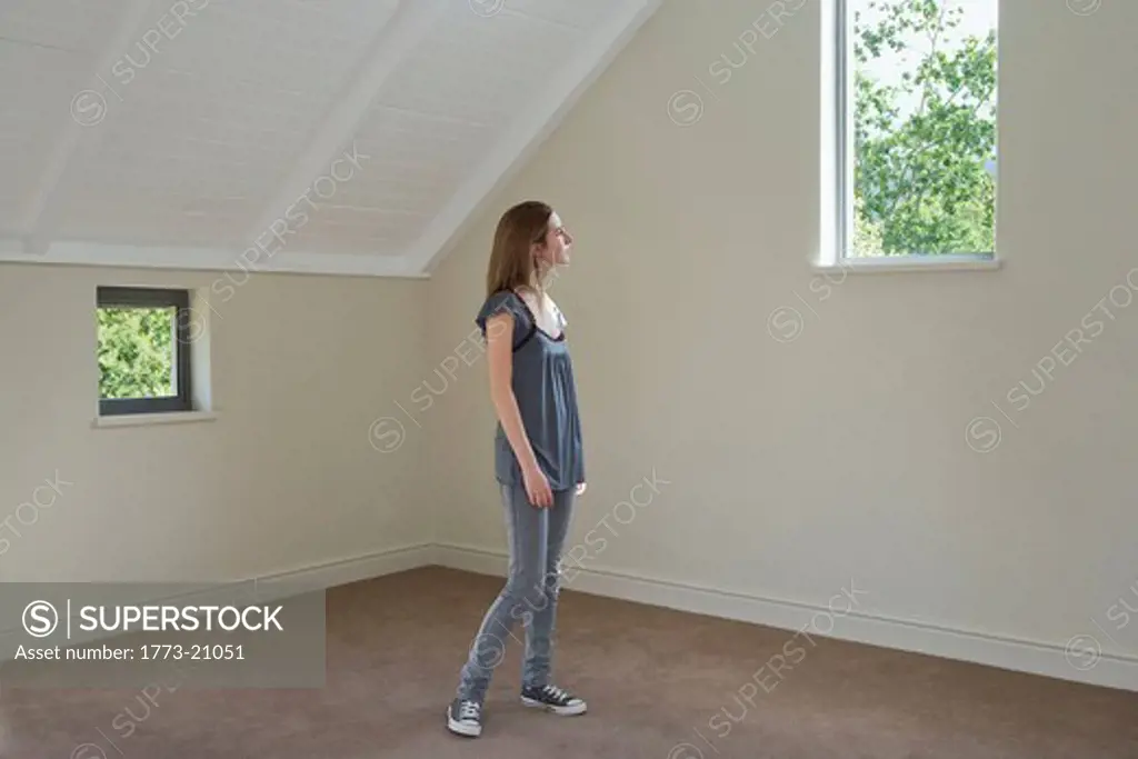 Woman standing in empty room looking at trees through window