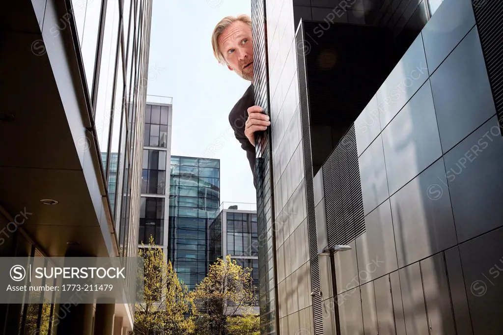 Oversized businessman peering from behind skyscrapers, low angle view