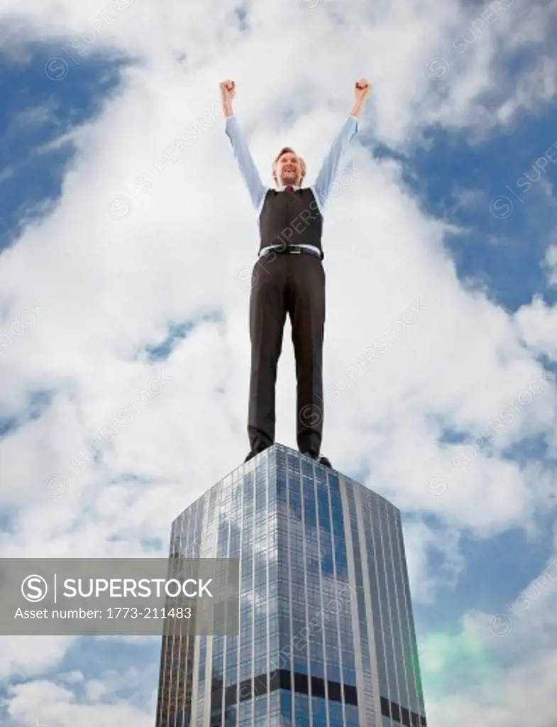 Oversized businessman cheering on skyscraper, low angle view