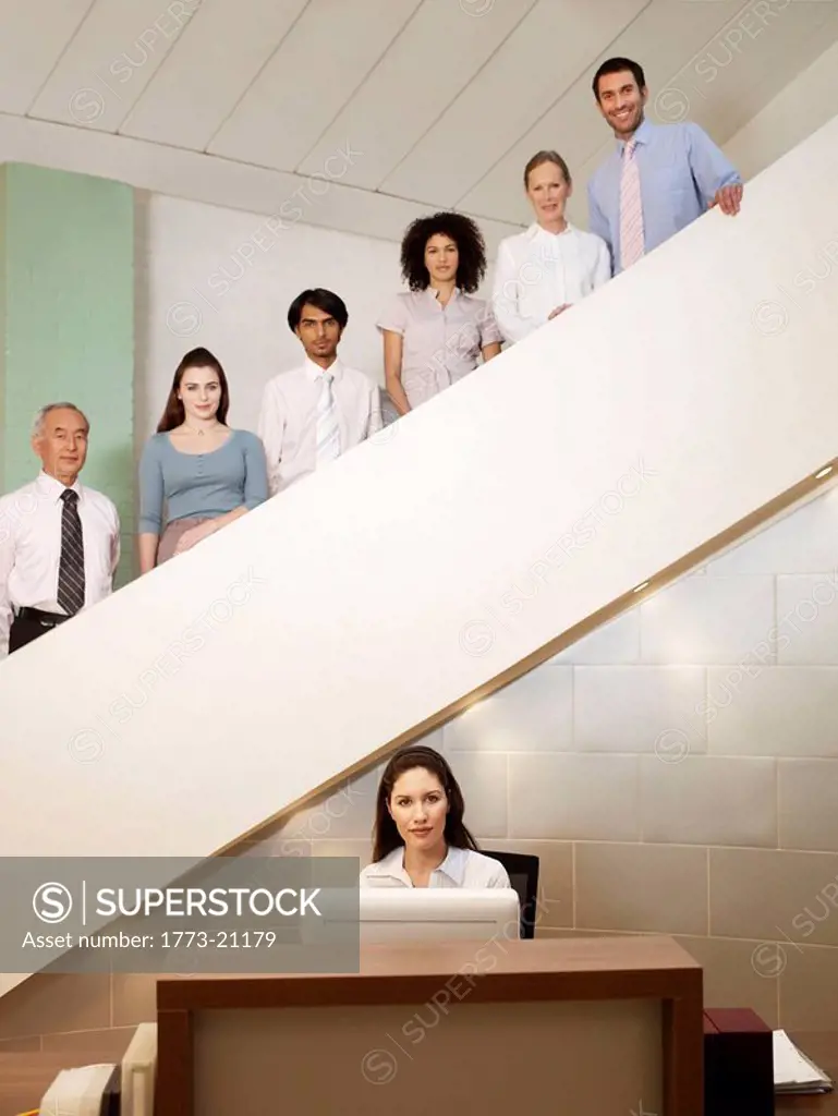 Six office workers of different ages posing on staircase behind a receptionist