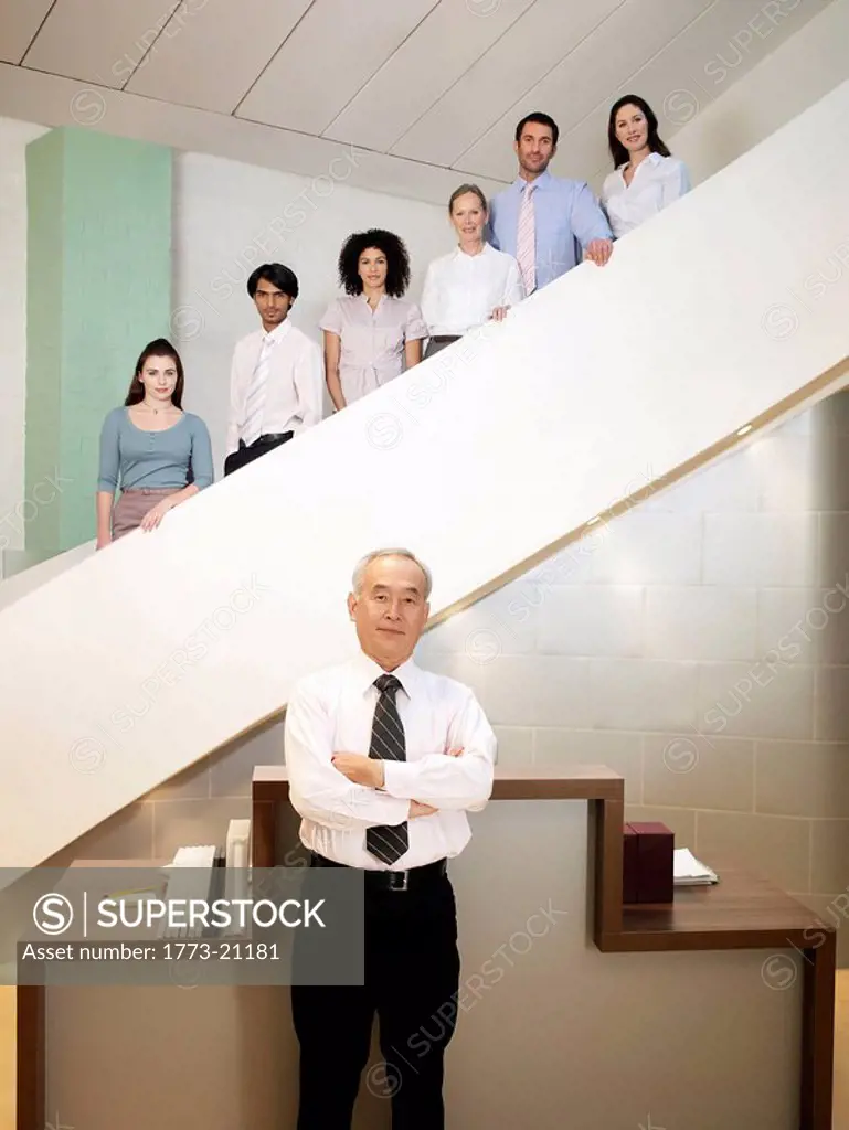Six office workers of different ages and sexes posing on staircase, senior man in forground