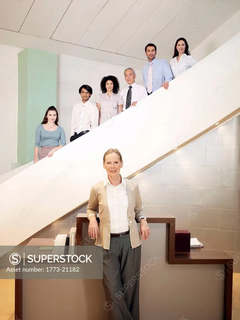 Six office workers of different ages and sexes posing on staircase, senior woman in forground