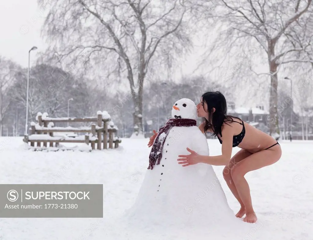 Woman in bikini kissing snowman