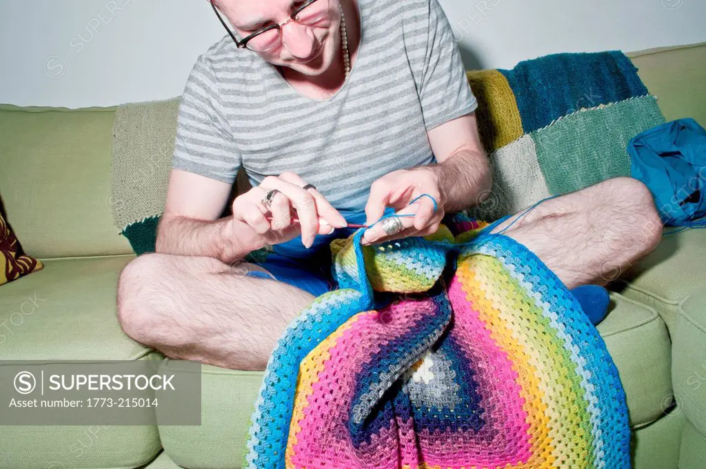 Mid adult man sitting on sofa crocheting