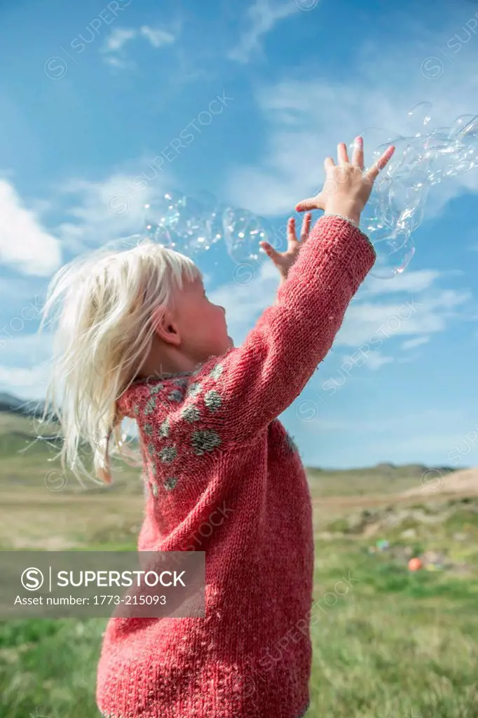 Young girl reaching to catch bubbles