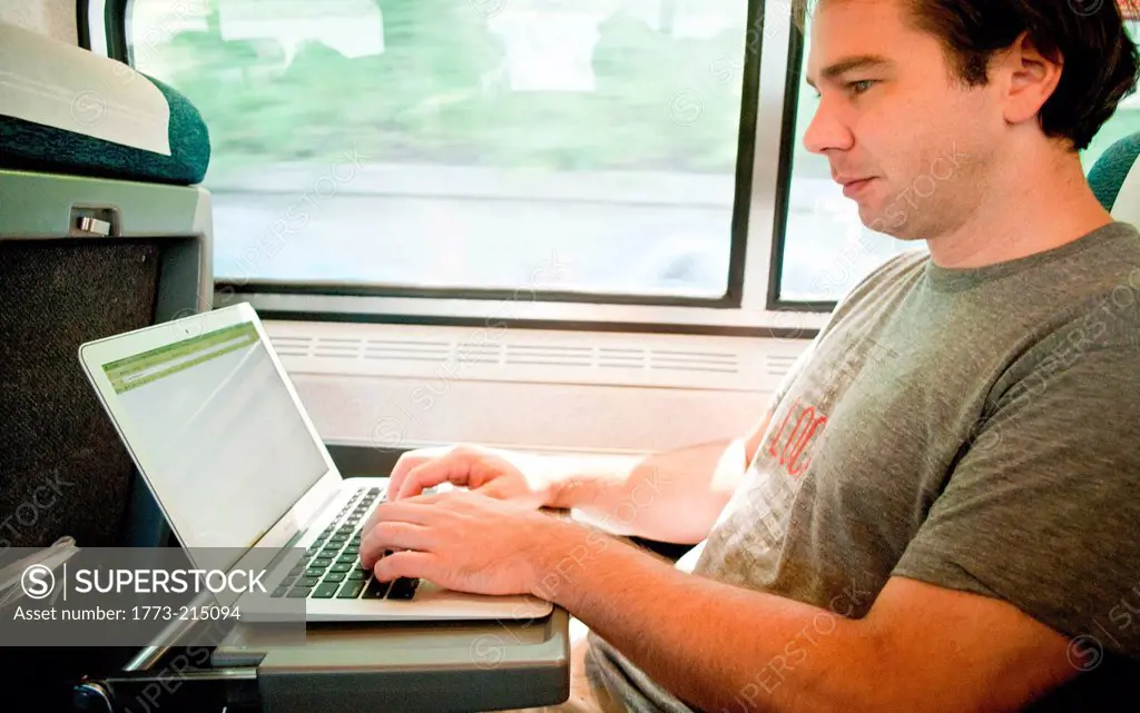 Mid adult man on train using laptop computer