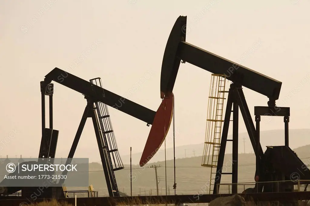 Oil pump jacks or nodding donkeys working in vast oil field in remote area