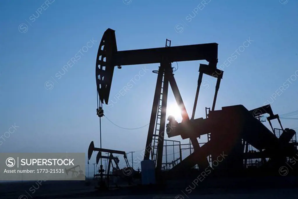 Oil pump jacks or nodding donkeys working in vast oil field in remote area at twilight
