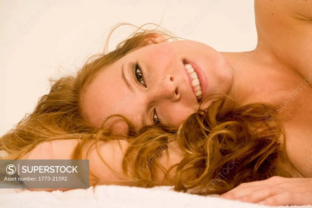 Blonde woman lying on towel with eyes open .horizontal side view.Studio lighting.White background,Close up of girl smiling