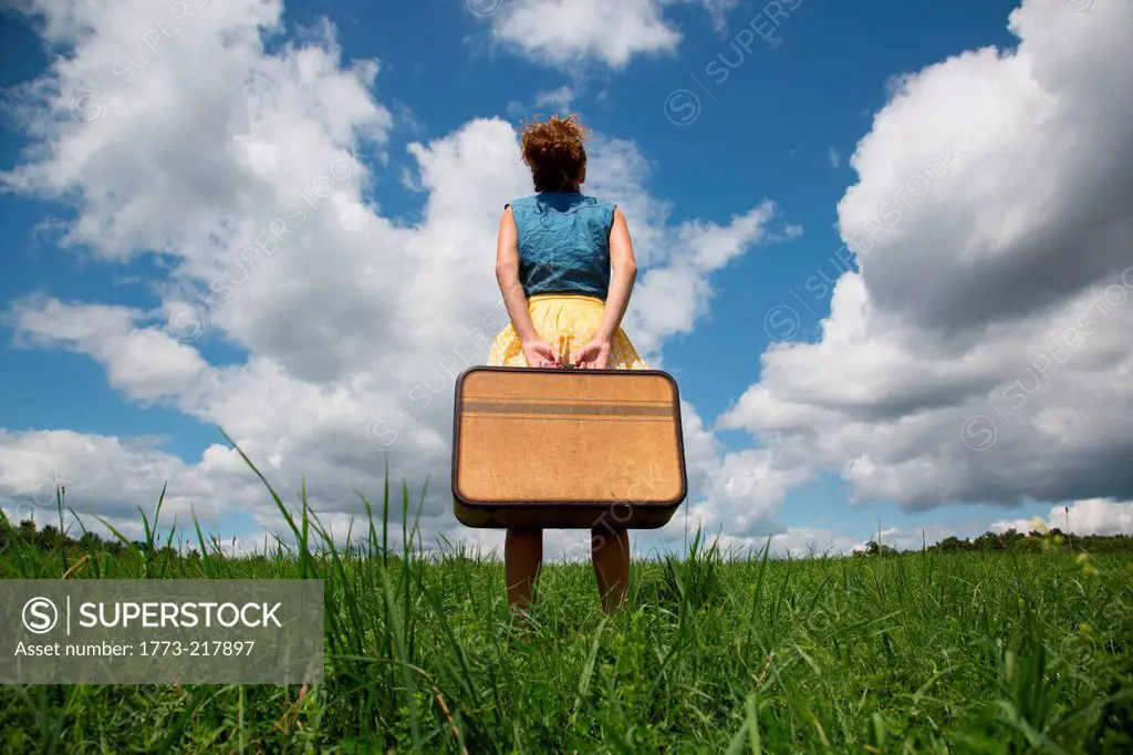 Teenage girl holding suitcase in field