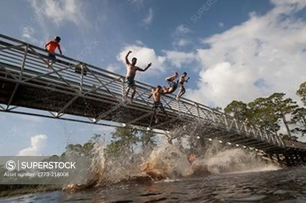 Boys and man leaping from footbridge, Miramar Beach, Florida, USA