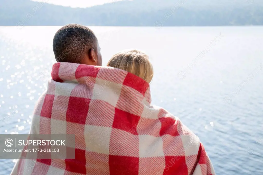 Young couple wrapped in blanket by lake, Hadley, New York, USA