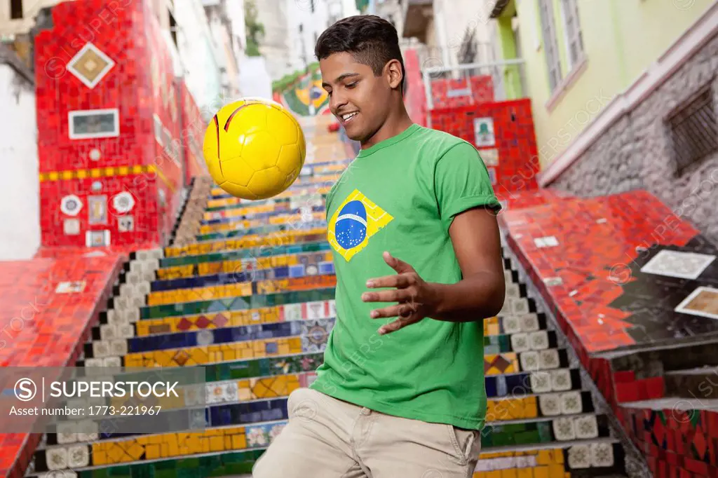 Young man wearing Brazil top doing keepy uppys in front of the Escadaria Selaron steps in Rio de Janiero, Brazil