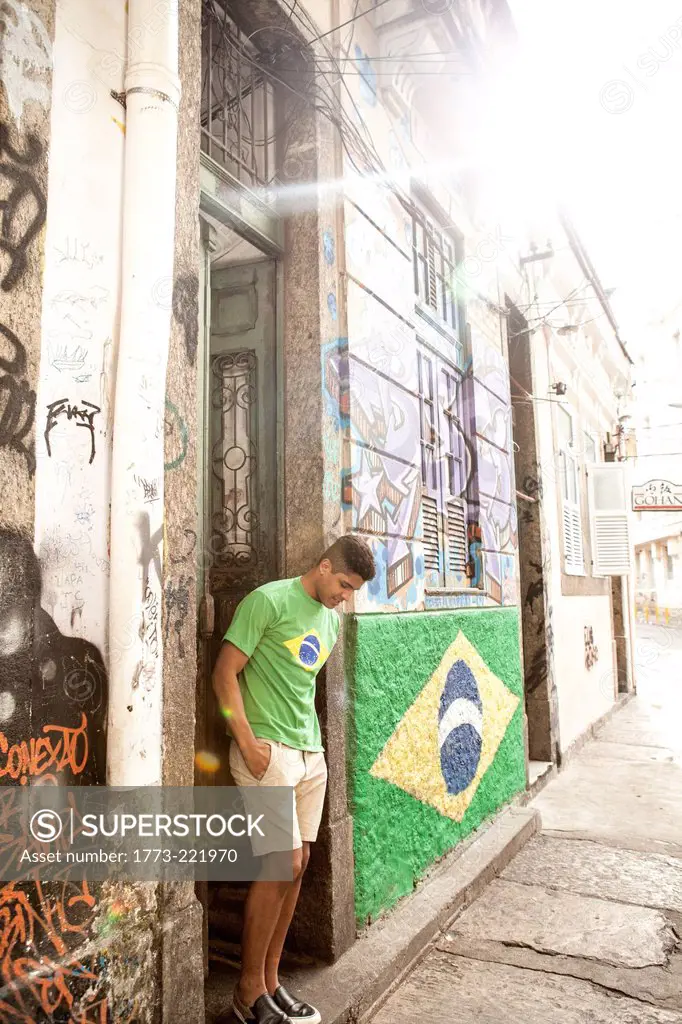 Young man wearing Brazil top standing in doorway next to Brazil flag