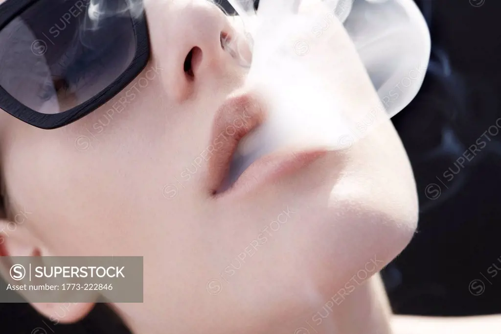 Studio head shot of young woman exhaling cigarette smoke