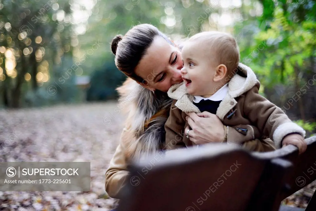 Mother holding male toddler on woodland park bench