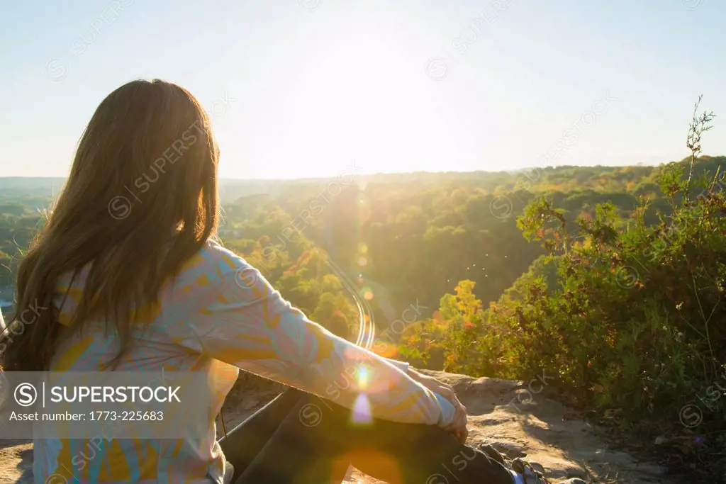 Mid adult woman sitting on elevated rock watching sunrise