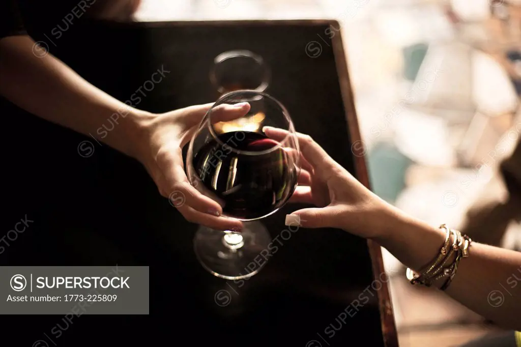 Close up of bartender serving glass of red wine to young woman