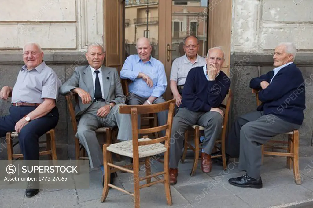 six old men sitting outside on chairs