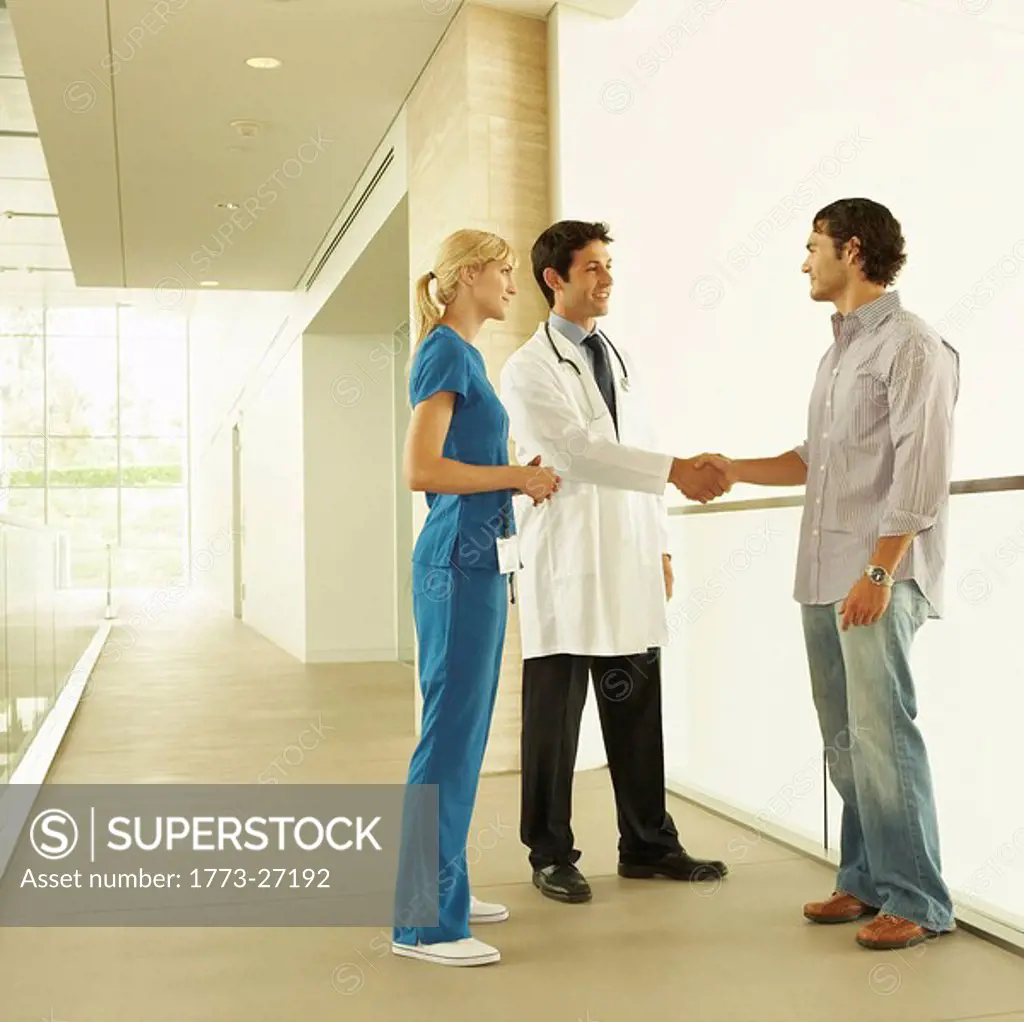 Doctor and nurse, wearing scrubs and lab coat, standing in hallway discussing care with patient or patient´s family in modern hospital or clinic