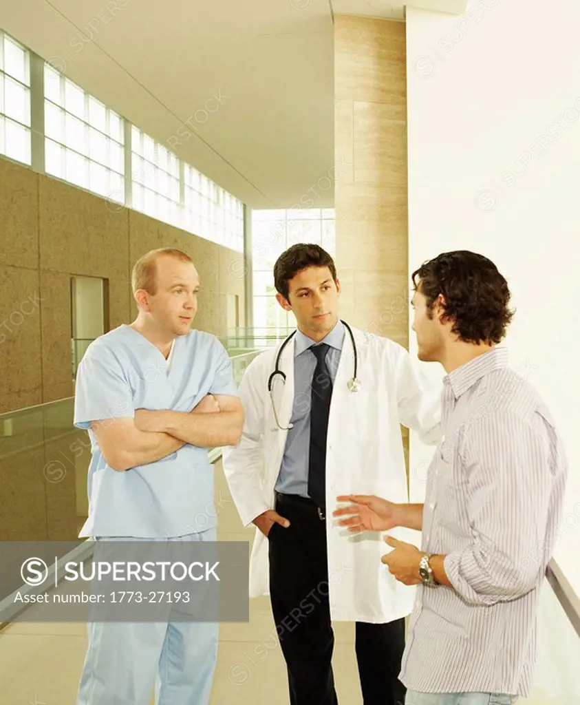 Doctor and nurse, wearing scrubs and lab coat, standing in hallway discussing care with patient or patient´s family in modern hospital or clinic