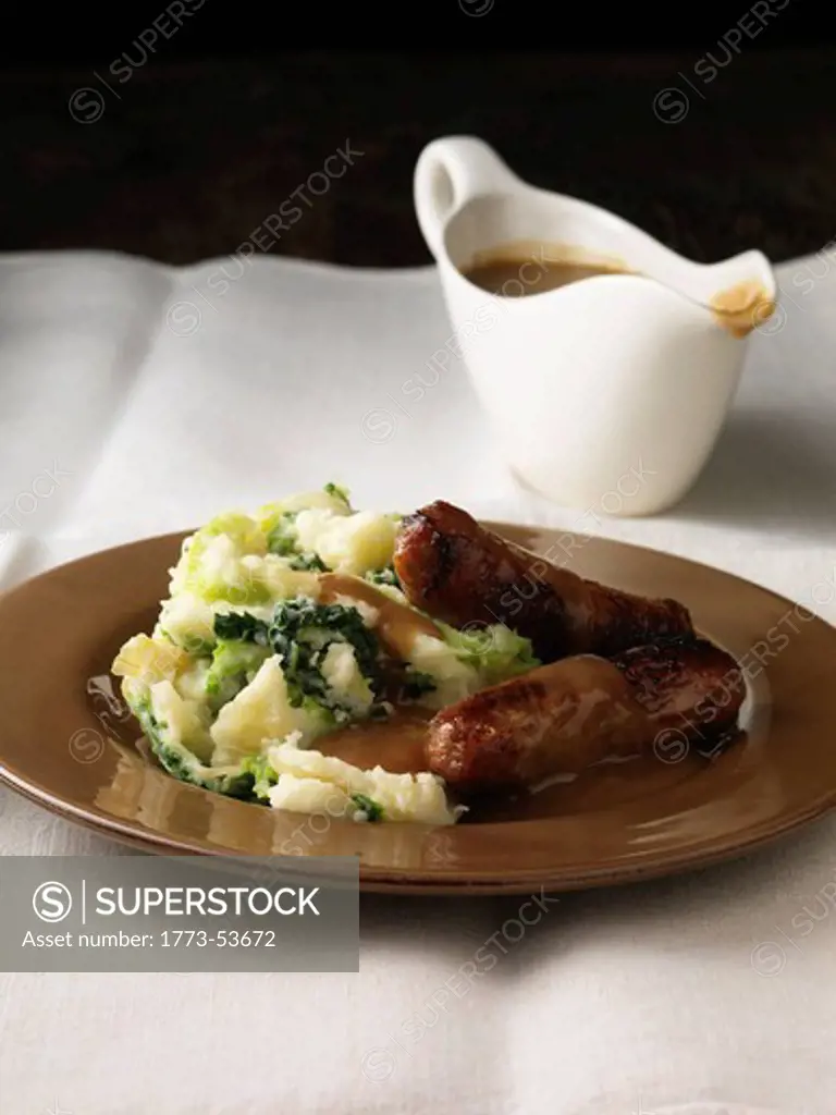 Sausages Bangers with Mashed Potato and gravy. Gravy boat in the background. All on a White  Table Cloth