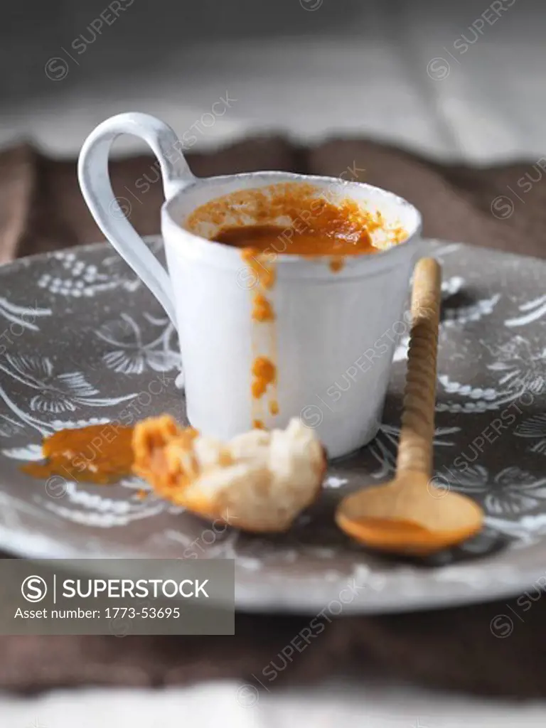 Tomato soup in little mug with bread 0n brown floral china plate with spoon and small pice of bread