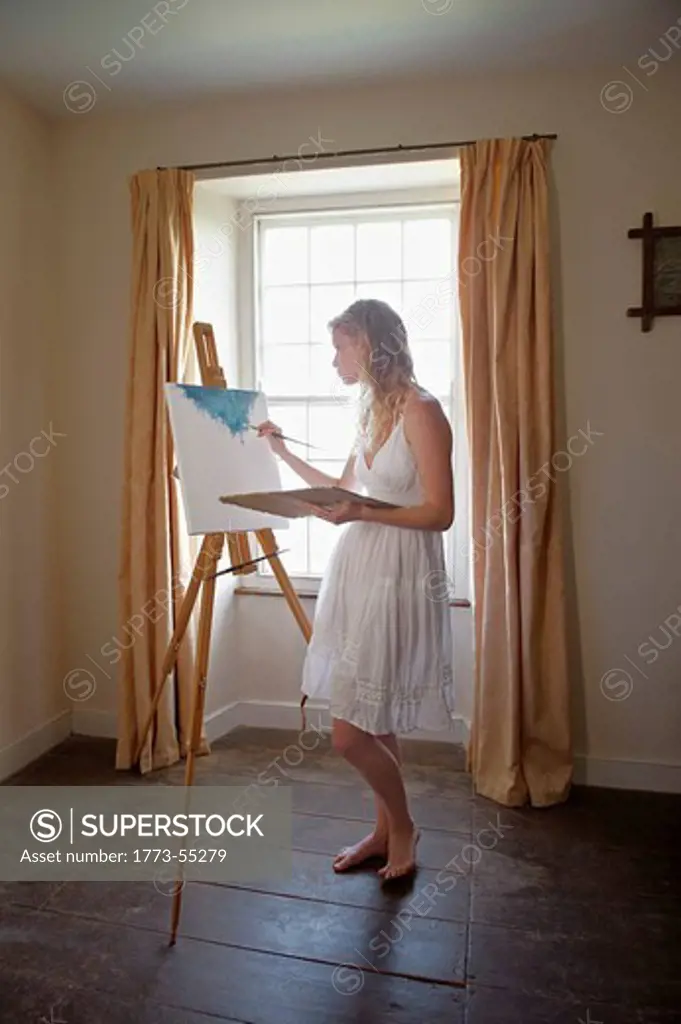 Young woman painting by window