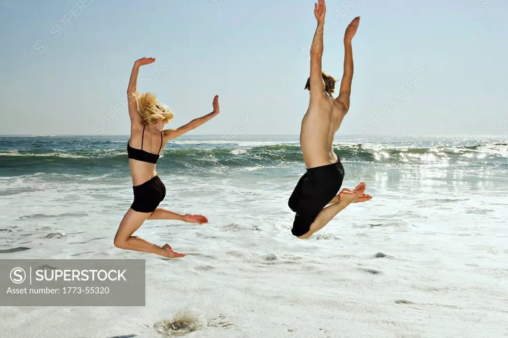 Couple leaping into waves on beach