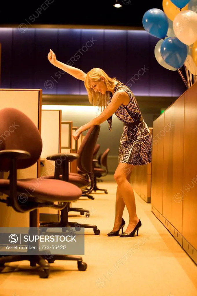Woman, at work late at night standing by cubicle in empty office, with arm raised in excitement, celebrating success