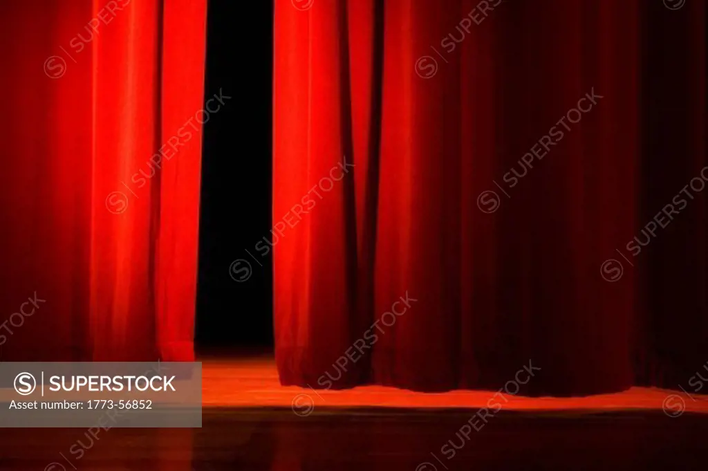 Red velvet curtains opening on lit stage in dark theater