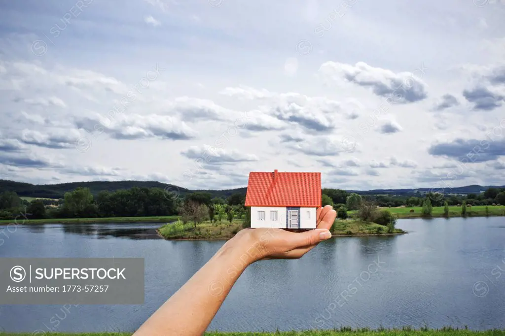Woman holding model house at lake